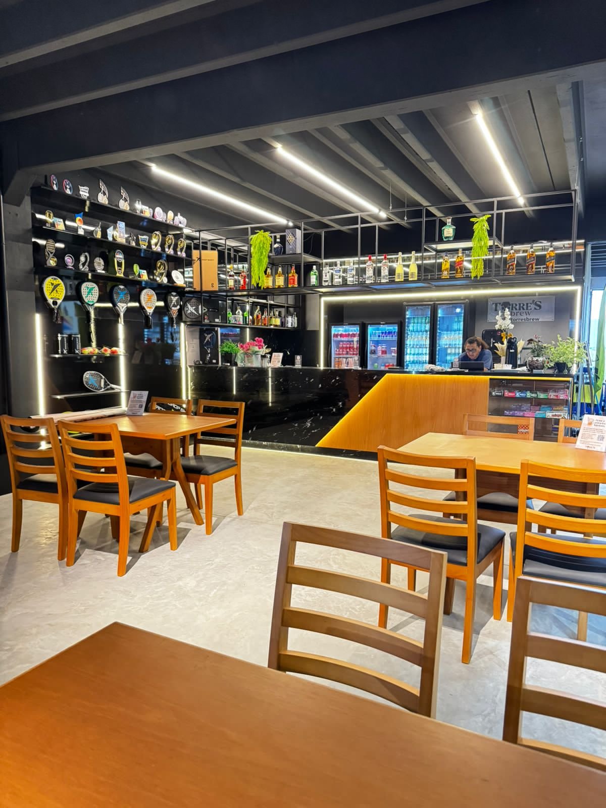 O bar da Arena 7: balcão com fita de LED, vitrine de raquetes, geladeiras de bebidas e mesas de madeira